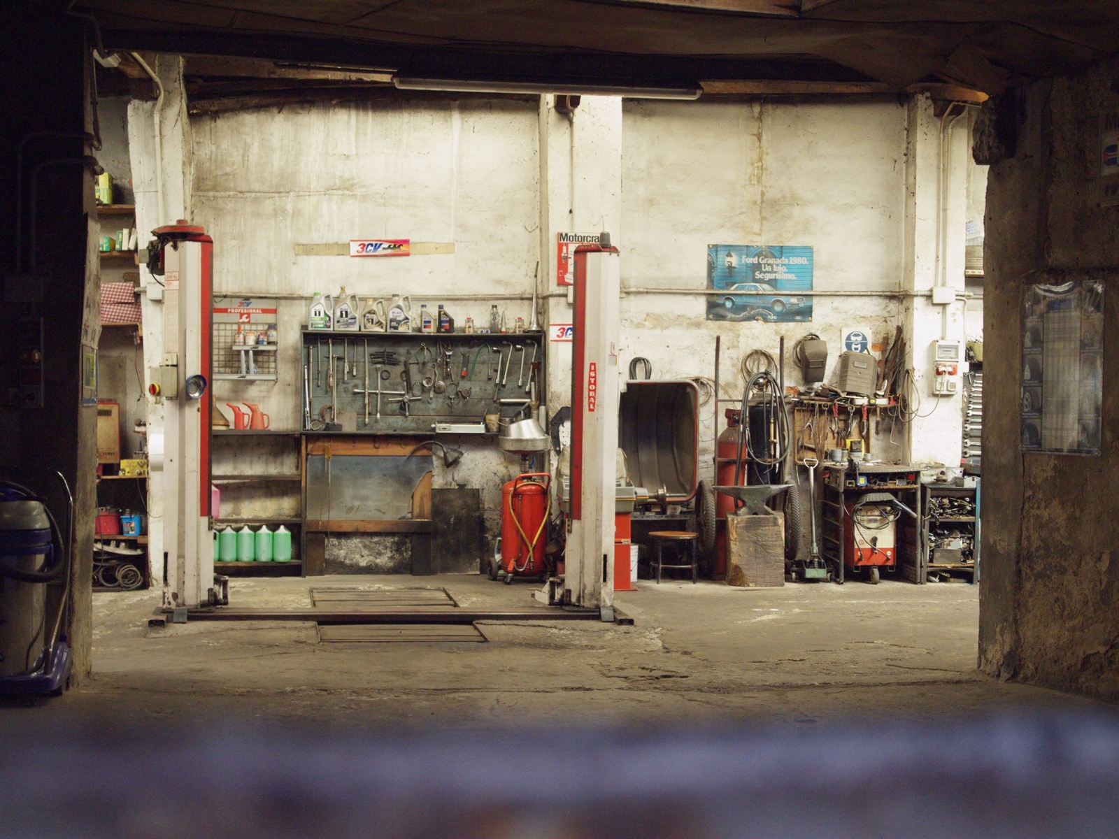 The inside of a single bay independent workshop: an empty two post lift, a tool wall and a worn concrete floor.