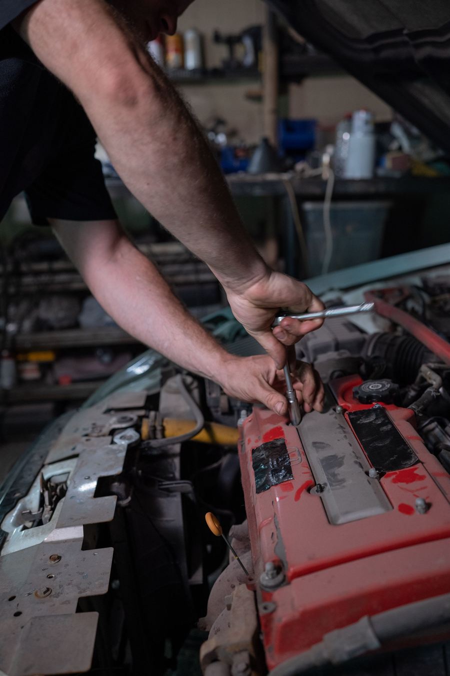 Hands reaching into an open engine bay with a long spanner.