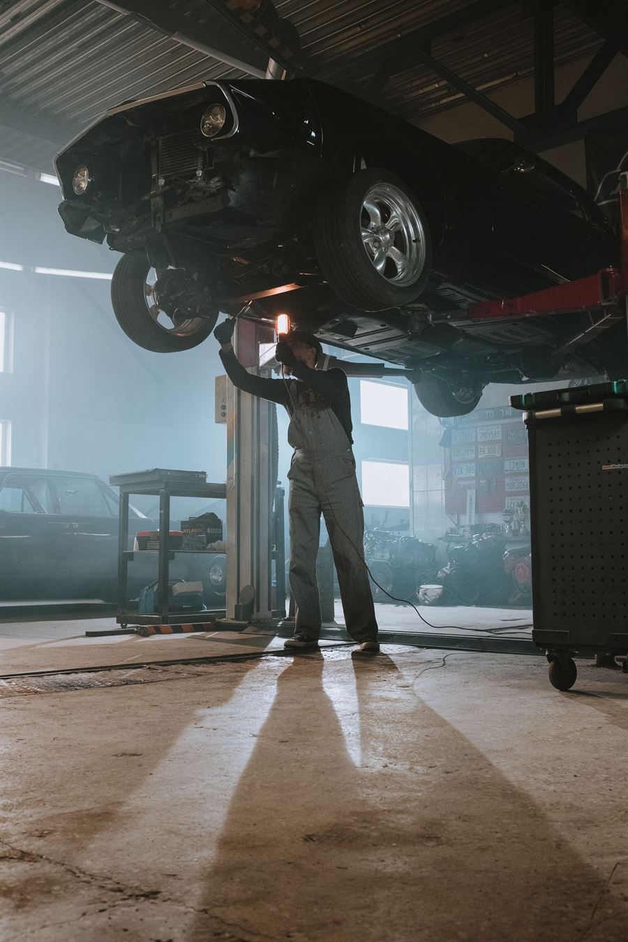 A car raised high on a two post lift, seen from the workshop floor.