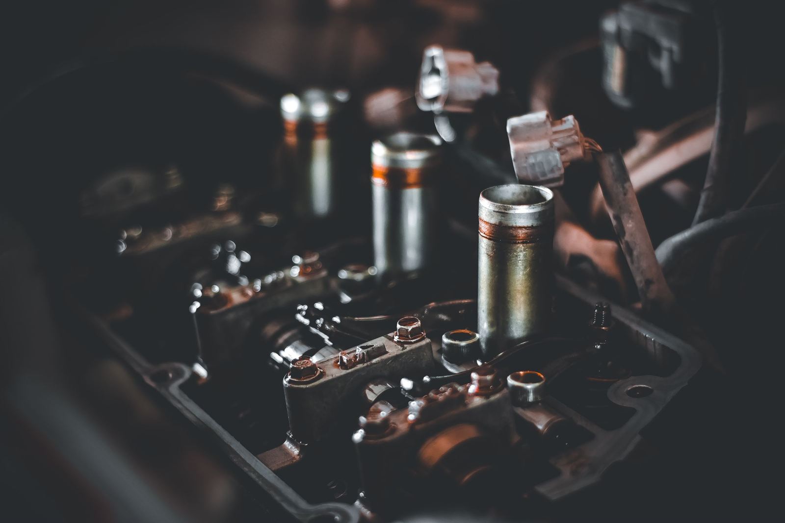 A close view of the top of an engine with the rocker cover off, spark plug wells and rocker gear in shadow.